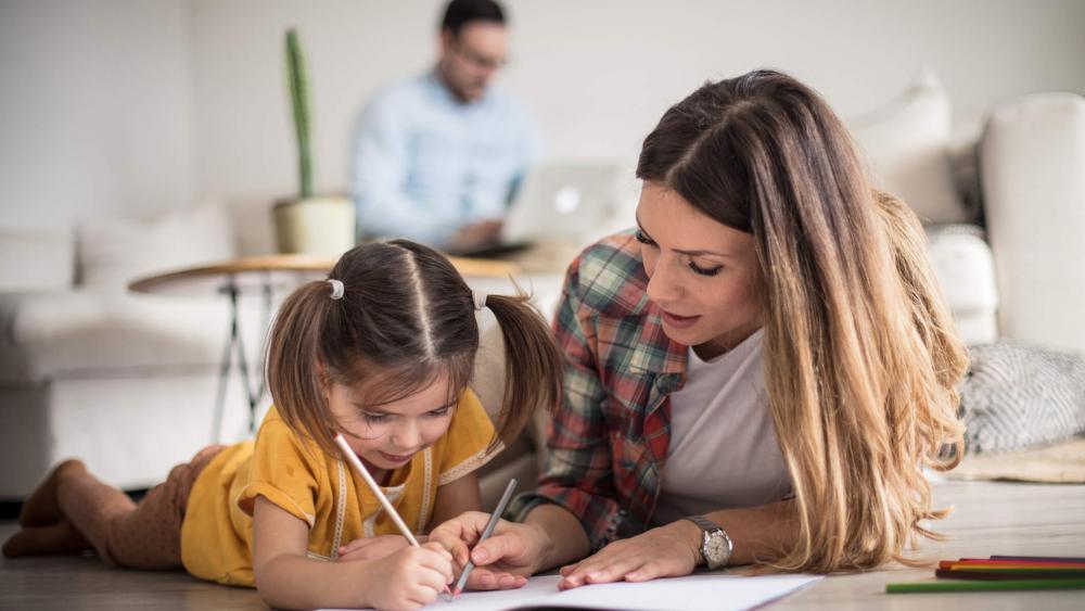 Little girl working her homework with mother.