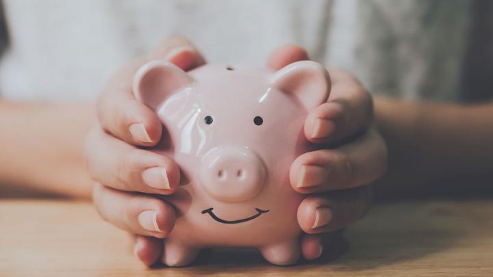 Panoramic image, Man hand holding piggy bank on wood table. Save money and financial investment