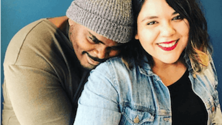 African American man hugging Latina woman from the back while both smiling