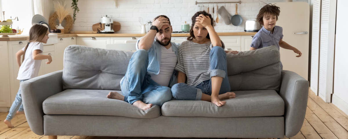 parents on sofa exhausted with kids running around